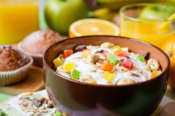 Healthy breakfast with yogurt, muesli and candied fruit in ceramic bowl on green wooden background
