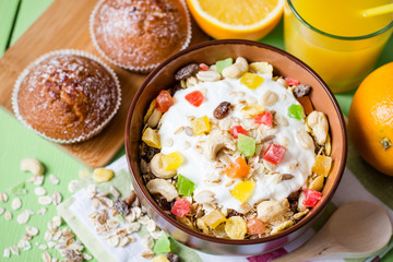 Healthy breakfast with yogurt, muesli and candied fruit in ceramic bowl on green wooden background