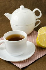 Obraz na płótnie Canvas on napkin cup of tea with lemon in saucer and teapot