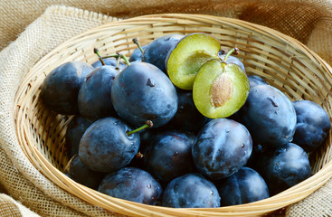 Many fresh Plums or Zwetschge and cut can see the seed in basket on wooden floor.