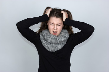 Portrait of upset the girl looks angry, her hands in her hair she tearing her hair and screaming  standing over gray background and looking at camera