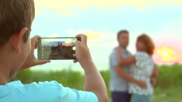 Little boy photographing with smartphone his parents outdoors. Slow motion 240 fps. Full HD