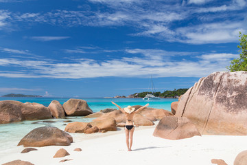 Fototapeta na wymiar Woman arms rised, wearing black bikini and beach hat, enjoying amazing view on Anse Lazio beach on Praslin Island, Seychelles. Summer vacations on picture perfect tropical beach concept.