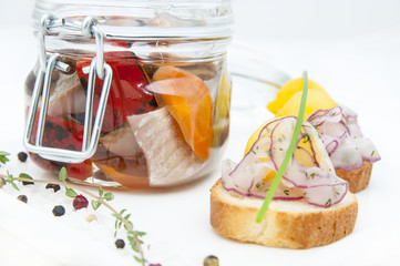 Pickled herring in a glass jar with potato canapes