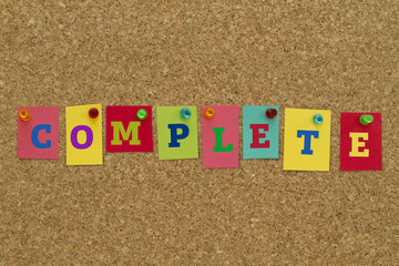 Complete word written on colorful sticky notes pinned on cork board.