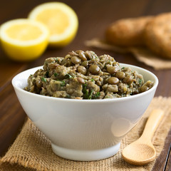 Lentil, parsley and lemon juice spread in bowl with wholegrain rolls and lemon halves in the back, photographed with natural light (Selective Focus, Focus in the middle of the spread)