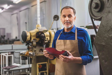 bearded shoemaker holding footwear and smiling