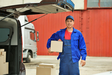 Delivery concept. Postman with parcel near a car