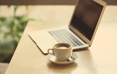 Aromatic cup of coffee and laptop on table in cafe