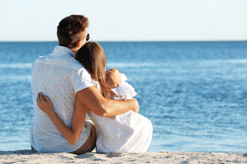 Happy couple sitting on sand on seashore