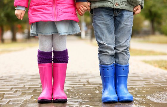 Close up view of children legs in gumboots standing on wet pavement