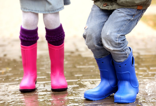 Close up view of children legs in gumboots jumping on wet pavement