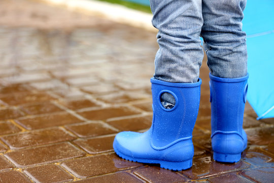 Close up view of boy in blue gumboots standing on wet pavement