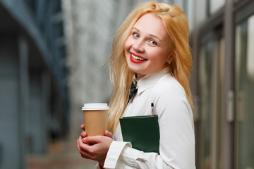 Smiling ginger with book and coffee in hand in building