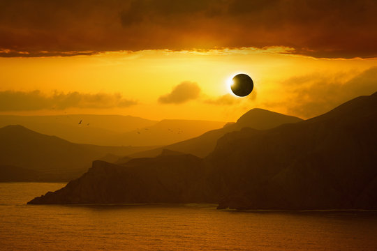 Total solar eclipse, silhouettes of mountains in red glowing sky