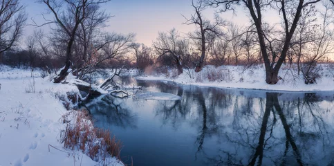 Zelfklevend Fotobehang Panoramisch winterlandschap met bomen, prachtige bevroren rivier bij zonsondergang. Winterbos. Seizoen. Landschap met winterbomen, water en blauwe lucht in de schemering. Ijzige besneeuwde rivier. Sneeuw. Reflectie in water © den-belitsky