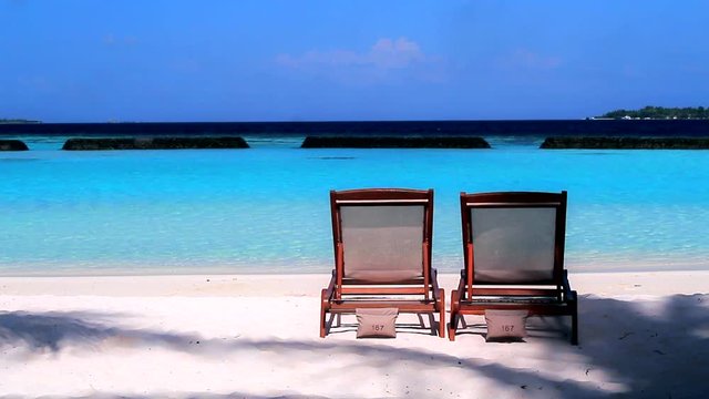 Two sun loungers at lonely island of Maldives with blue sky and cristal clear water
