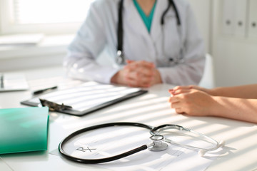 Stethoscope next to hand of doctor  reassuring her female patient. Medical ethics and trust concept