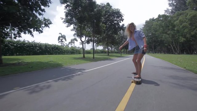 REAR POV WS Blonde young woman skateboarding down road