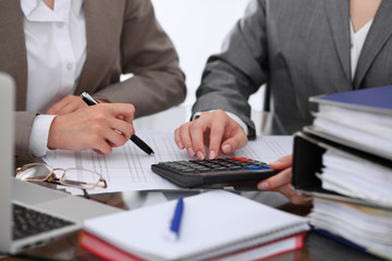 Two female accountants counting on calculator income for tax form completion hands closeup....
