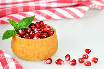 Pomegranate seeds in a wooden bowl on light background