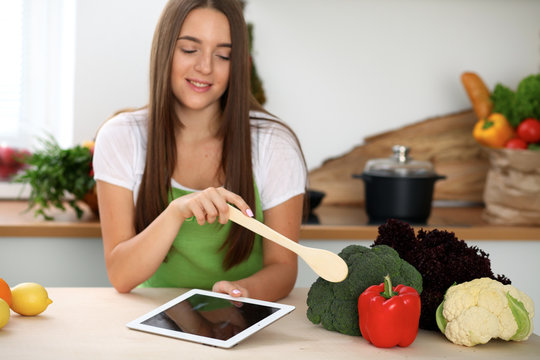 Young woman is going to cook healthy meal from vegetables. Close up of housewife with wooden spoon pointing into pepper and brocolli. Vegetarian concept.