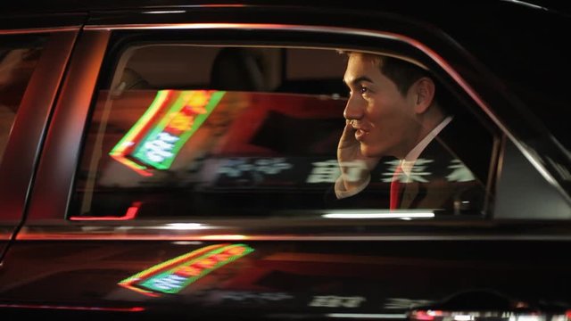 MH LD Businessman Sitting in Car Talking on Phone with Reflections of Chinese Characters on Window / Singapore