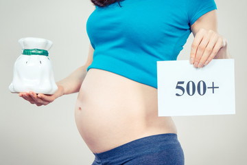 Pregnant woman holding piggy bank and inscription 500+, social program and policy in Poland