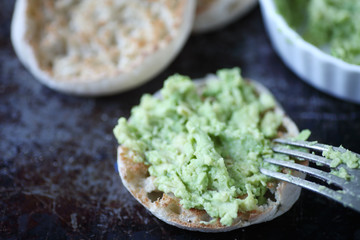 Toasted English muffins with mashed avocado on metal surface