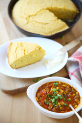 A bowl of chili with wedge of cornbread and butter