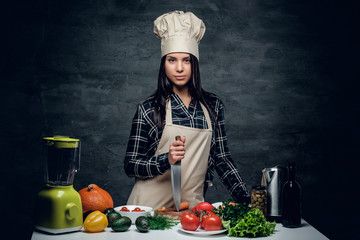 Female chef holds a knife and posing near a table with fresh veg