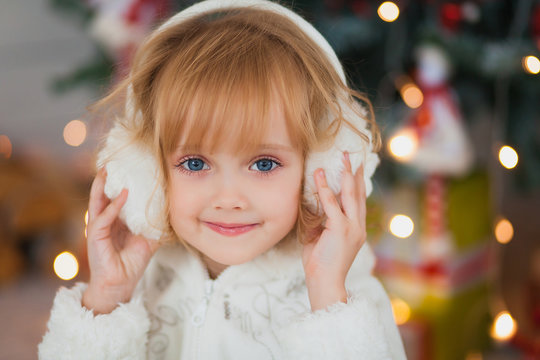 Little beautiful girl in warm white headphones around the Christmas tree