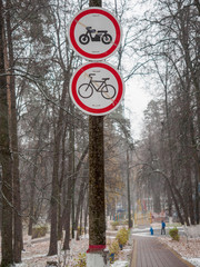 Path, wet after snowfall, in the park with prohibition signs for motorcyclists and cyclists.