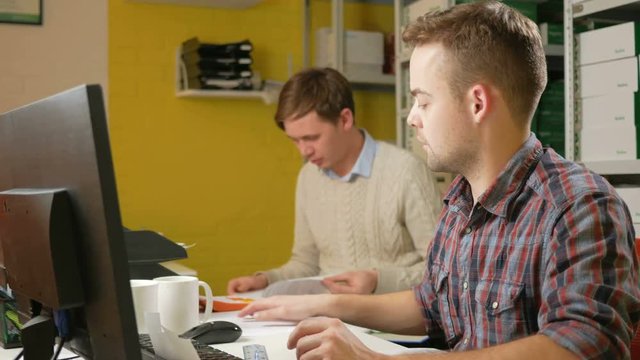 A young team of men working on a project in the office at the computer. Check the documents on taxes and fill out the electronic form. Teamwork to solve problems