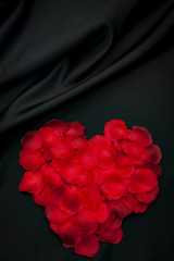 Valentine’s day concept with red rose petals arranged to resemble a heart with copy space on black silk background