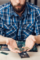 Computer microchips in male hands, close-up. Unrecognizable bearded repairman holding components. Electronic repair shop, laptop disassembling, technology fixing concept