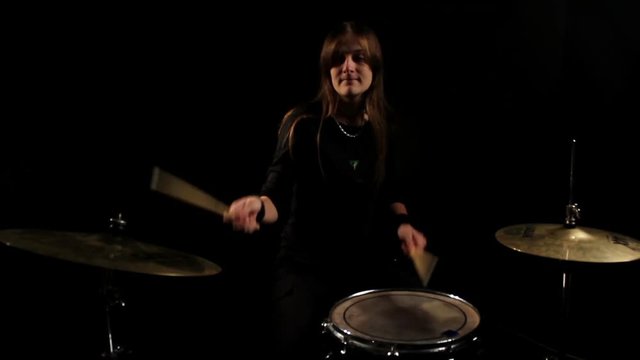 woman drummer playing on drums in a dark room