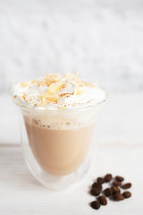 Close-up of cappuccino cup with coffee beans on white background. Tasty appetizing creamy latte in glass mug. Dessert, restaurant serving, hot beverage concept
