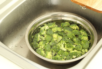 Washing broccoli in the kitchen sink.