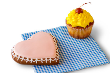 Heart biscuit and yellow cupcake. Pastry on checkered napkin. Surprise for those you love. Find an occasion for holiday.