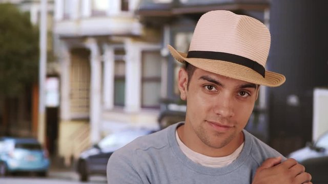 Handsome millennial Latino mixed race man standing on city street with hat. Fashionable young Mexican man in 20s wearing fedora