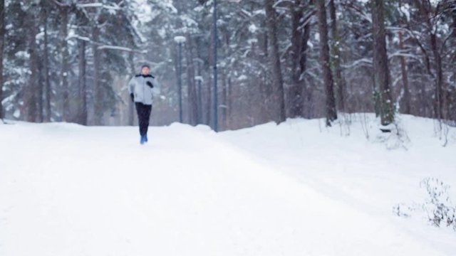 man running on snow covered winter road in forest 