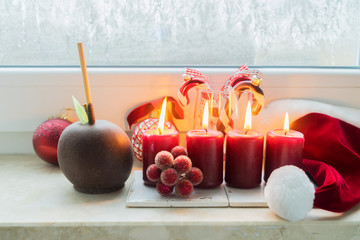 Christmas scene with red burning candles and chocolate apple on windowsill