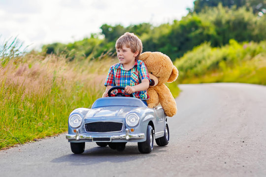 Naklejki Little kid boy driving big toy car with a bear, outdoors.