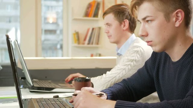 Young man working in the office of the laptops on the project. Focused typing on keyboard and looking at the screen. The concept of teamwork