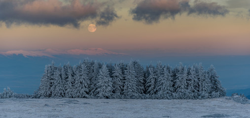 Amazing pink purple winter sunset in the mountains - beautiful frozen landscape - moon rising over...