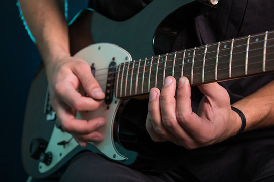 Young man playing electric guitar on dark background