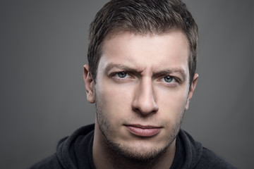 Obraz premium Close up moody portrait of distrustful young man looking at camera