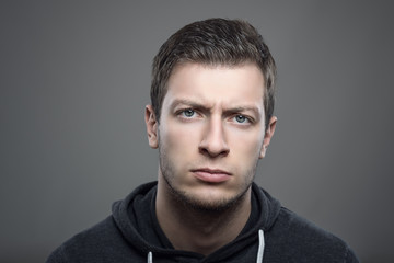 Moody headshot portrait of young upset man in hooded shirt looking at camera