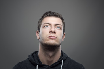 Moody portrait of young casual man looking up with illuminated face over gray background